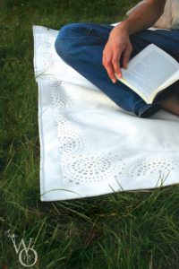 detail of white felt picnic rug in grass.