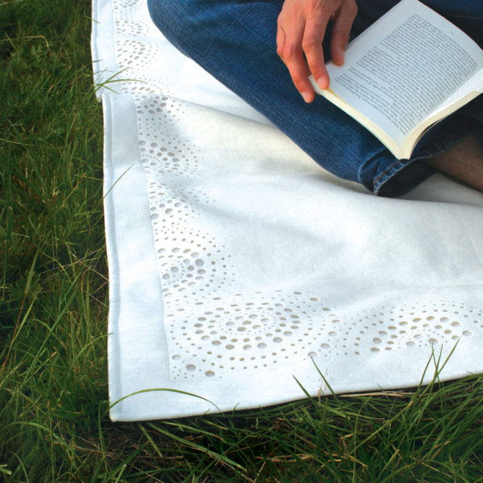 detail of white felt picnic rug in grass.